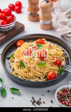 Fetapasta, spaghetti with baked feta with cherry tomatoes and herbs in a black plate. Vertical view. Stock Photo