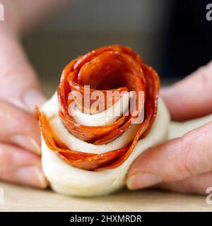 woman is making rose-shaped pepperoni snack. pastry with salami. homemade puff pastry ready to bake. Stock Photo