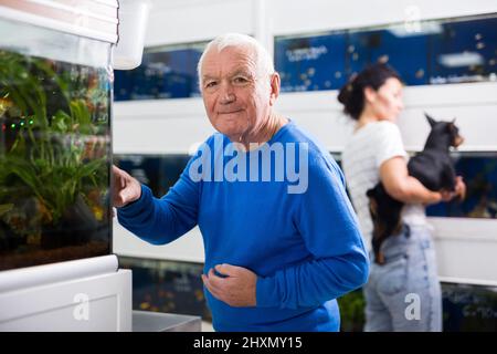 Positive mature man chooses aquarium fish in pet shop Stock Photo