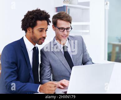 Putting their heads together for a solution. Shot of two male colleagues working together on a laptop. Stock Photo
