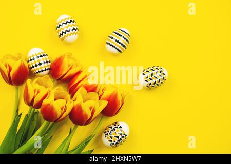 Golden, white, geometric easter eggs with tulips on a yellow background. Geometry. Minimal easter concept. View from above Stock Photo
