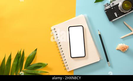 Smartphone white screen mockup on a workspace with summer compositions on yellow and blue background. Camera, starfish, diary, plan, seashell. top vie Stock Photo