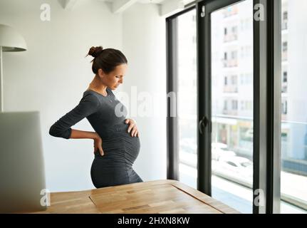 Any day now.... Shot of a pregnant businesswoman standing in her office holding her stomach. Stock Photo