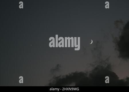 The crescent moon in the cloudy sky, rising in the east Stock Photo