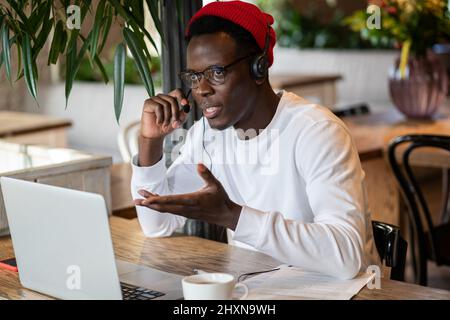 Confident African American freelancer man talking in headphones using laptop, making video call Stock Photo