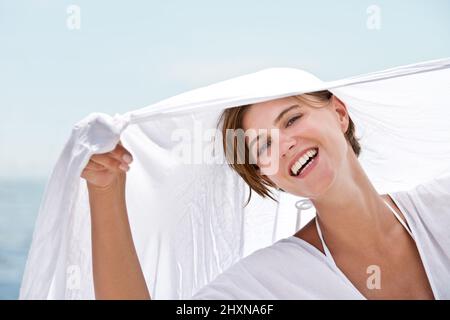 Without a care in the world.... A beautiful young woman holding a white sarong thats blowing in the wind. Stock Photo
