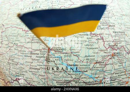 close up birds eye view of the Ukrainian blue yellow flag stuck in a map showing the capital Kyiv and the word Ukraine. Shows location and cities Stock Photo