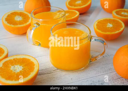 Oranges and fresh-squeezed orange juice close up on light wooden background Stock Photo