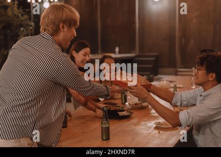 Young Asian friends eating and enjoying dinner together at outdoor restaurant. Friendship and reunion celebration Stock Photo
