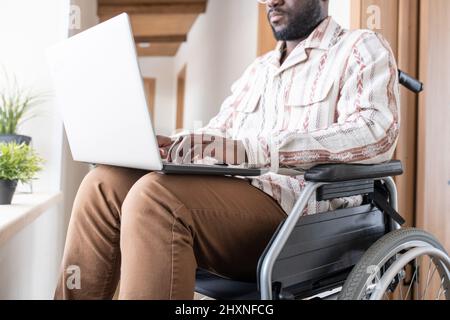 Close-up of young man with disability working in the net in home office while sitting in wheelchair in corridor of modern apartment Stock Photo