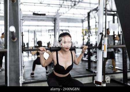 exercise concept The woman in black sport outfits carrying doing weight machine by carrying it on her shoulders and trying to lift it up. Stock Photo