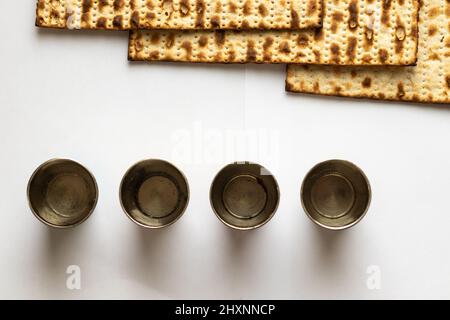 Three matzahs - Jewish bread for Passover. Next to four little silver cups. White background Stock Photo