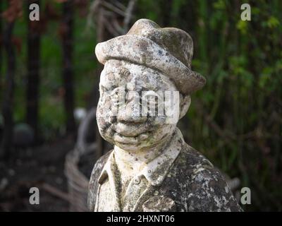 Close up photo of a hard weathered concrete statue, man in suit with hat Stock Photo