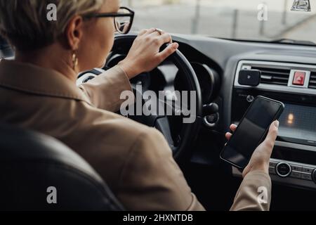 Business Woman Using a Smartphone While Driving Car, View from Back Seat Stock Photo