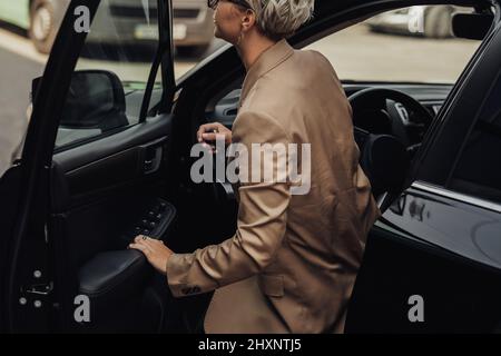 Woman Dressed in Rumpled Brown Jacket Getting of from the Car Stock Photo