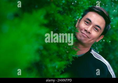 Asian man smiling with happy face standing in green bush for good mental health concept. Stock Photo