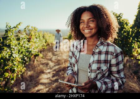 Mixed race female smiling while holding digital tablet working in vineyards with male colleague Stock Photo