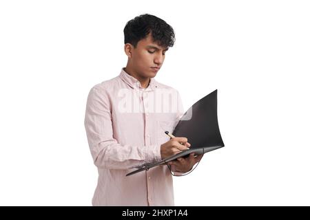 Young peruvian man writing on a folder with a pen, isolated. Stock Photo