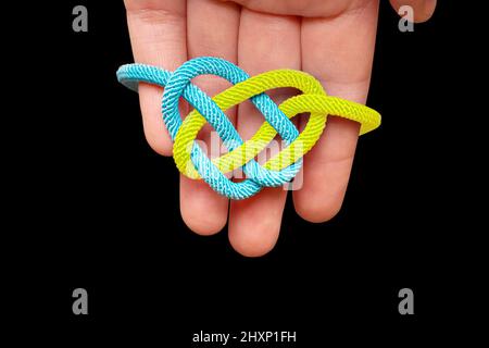 Heart shaped celtic knot painted the colors of the national flag of Ukraine in hand isolated on black background. Unity, faith and protection concept. Stock Photo