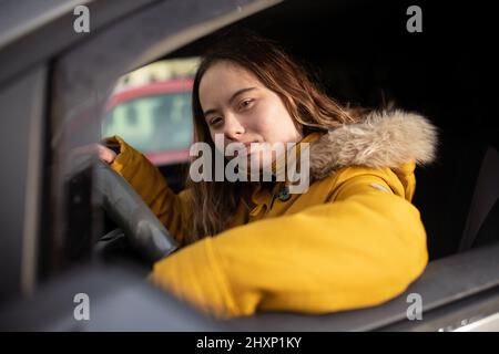 Young woman with Down syndrome driving a car and looking at camera. Stock Photo