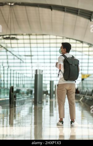 Young male wearing face mask with bagckpack walking in airport, protection Coronavirus disease infection, Asian man traveler. Time to travel after vac Stock Photo