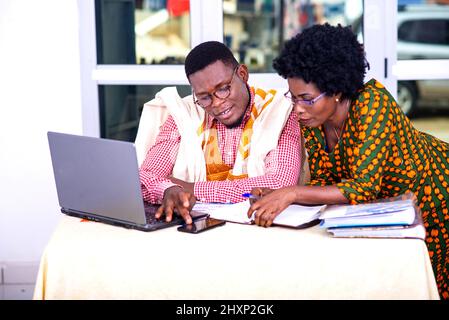 businessman and businesswoman sitting at laptop and working on mobile phone together in office. Stock Photo