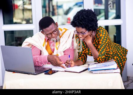 businessman and businesswoman working at laptop and checking reports on paper together in office. Stock Photo