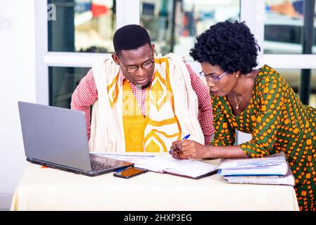 businessman and businesswoman working at laptop and checking reports on paper together in office. Stock Photo