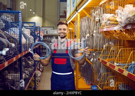 Happy salesman at hardware store standing in the aisle and showing hoses for washing machine Stock Photo