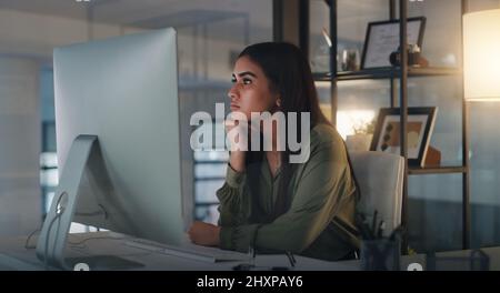 Searching for a little more inspiration. Shot of a young businesswoman looking thoughtful while working on a computer in an office at night. Stock Photo