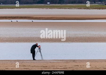 Lone photographer sets up his camera on its tripod on the sands of the river Kent estuary at Arnside in Cumbria. Stock Photo
