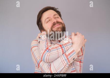 Caucasian man with beard hugging oneself happy and positive, smiling confident. Stock Photo