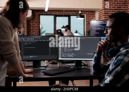 Multiethnic cyber security team members in agency office writing cloud database processing algorithm. Software developers sitting at desk and developing a functional data encryption system. Stock Photo