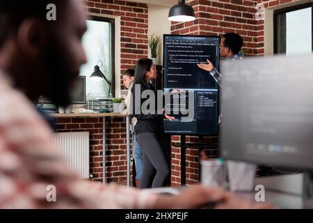 Software developers standing near vertical screen talking about interface bug and slow rate of processing data. Cybernetics engineers reviewing lines of code in order to secure mainframe database. Stock Photo