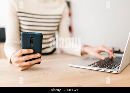 Close up woman hands using mobile phone and laptop in home office Stock Photo