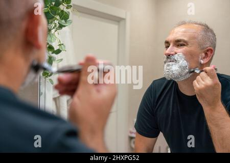 Shaving off beard and mustache. Man using razor to get rid of hairs on his face Stock Photo