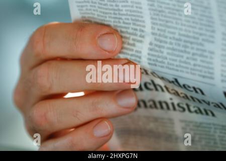 Man's hand holding newspaper. Text unreadable Stock Photo