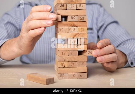 Planning, risk and strategy in business. Wood blocks tower in businessman hands closeup. Man taking brick out of stack. High quality photo Stock Photo