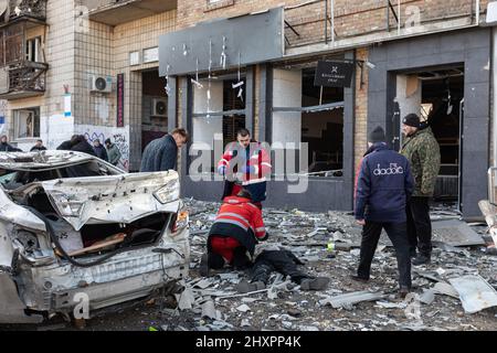 KYIV, UKRAINE - Mar. 14, 2022: EDS NOTE: GRAPHIC CONTENT, KYIV, UKRAINE - Mar. 14, 2022: War of Russia against Ukraine. The killed civilian lies on the sidewalk in front of the civilian house damaged by rocket attack the city of Kyiv Stock Photo