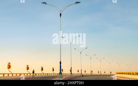 Curve road with street lamp pole and yellow curve traffic sign. Back view of a man running on footpath beside empty road. Red-white prohibited stop Stock Photo