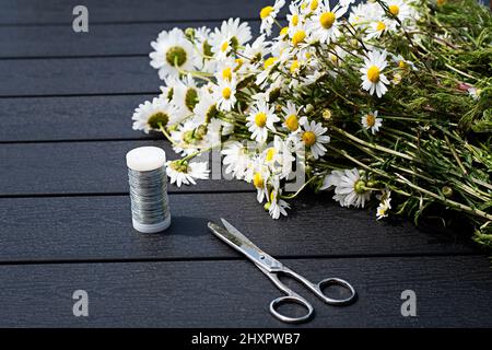 Wild flowers, wire and scissor on wooden table outdoors. Time to create a flower bouquet or flower crown. Photo taken on Midsummer Eve in Sweden. Stock Photo