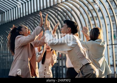 Group of excited Asian entrepreneurs giving high five to each other and celebrating success at party Stock Photo