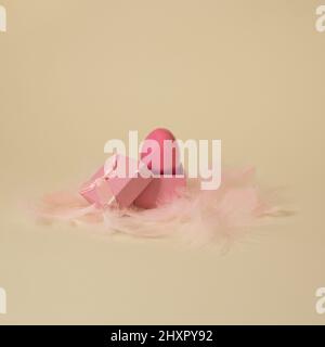 Bright pink Easter egg in gift box with feathers on yellow golden background Stock Photo