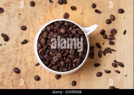 Top view of white coffee cup filled with whole coffee beans on wood table Stock Photo