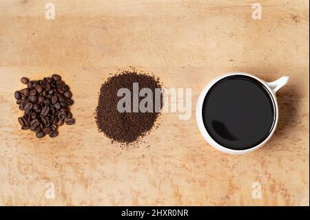 Whole coffee beans, ground coffee, and cup of brewed black coffee on wood table, top view Stock Photo