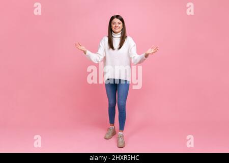 Full length portrait of happy woman outstretching hands to embrace, giving free hugs and welcoming, wearing white casual style sweater. Indoor studio shot isolated on pink background. Stock Photo