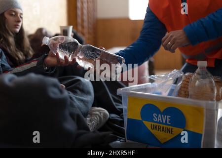 Ukrainian war refugees in temporary shelter and help center getting drinks from volunteers. Stock Photo
