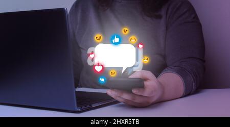 Young woman sending text messages with her smartphone. Hologram emojis with tactile screen  mobile. Stock Photo