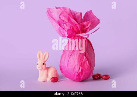 Chocolate Easter egg wrapped in paper and bunny on lilac background Stock Photo