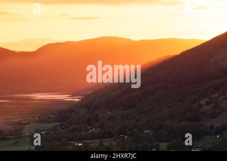 Beautiful golden rays of light from the evening setting sun shining through mountains into valley. Keswick, Lake District, UK. Stock Photo